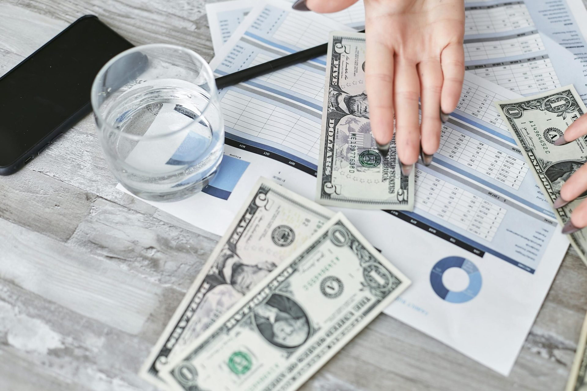 A top view of financial documents with dollar bills and a glass of water, emphasizing budgeting.